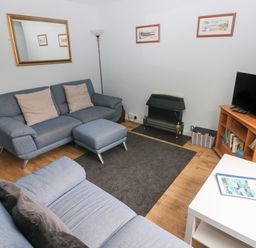 A living room with blue sofas a black fireplace a television on a wooden stand and a white table at Kittiwake Apartment 22 in Little Haven near Broad Haven