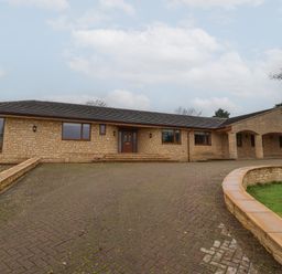A stone building with a paved driveway and covered entrance at Blossom Hill near Witney