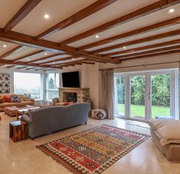A living room with wooden beams on the ceiling a stone fireplace multiple sofas a patterned rug and glass doors opening to a garden at Blossom Hill near Witney