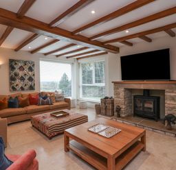 A living room with wooden ceiling beams a stone fireplace and a large corner sofa at Blossom Hill near Witney