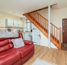 A sitting area with a red sofa next to a kitchen and wooden staircase at Badgers Sett in Stibb near Kilkhampton