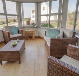 A seating area with woven chairs and a table by large windows at Horn Head View in Carrigart County Donegal