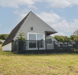 An exterior view of an a-frame house with a black fenced porch on a grassy area at La Bella Vista in Kilkhampton