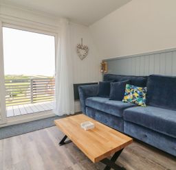 A living room with a blue sofa a wooden coffee table and large sliding glass doors at La Bella Vista in Kilkhampton