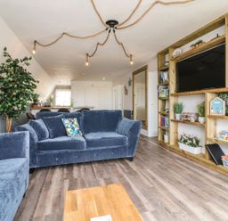 A living room with blue sofas wooden shelves with plants and decor and rope lighting at La Bella Vista in Kilkhampton