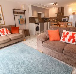 A living room with a sofa and kitchen area at The Packing House in Rosudgeon