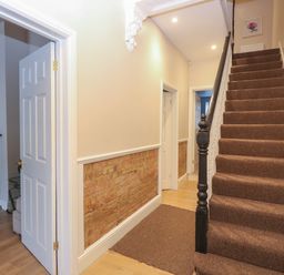 A hallway with carpeted stairs and exposed brick lower walls at Grosvenor House in Kirkley Rise