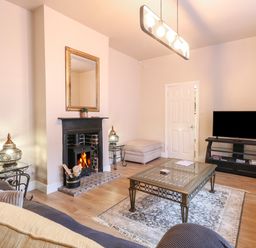 A living room with a fireplace a wall mirror a television on a stand a glass coffee table two sofas and two side tables Grosvenor House Kirkley Rise