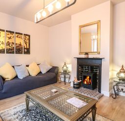 A living room with a blue sofa and cushions a coffee table a fireplace with a mirror above and decorative lamps on side tables at Grosvenor House in Kirkley Rise