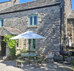 An outdoor area with a stone house, table, umbrella, and grill at The Old Farmhouse at Brackenthwaite Farm Yealand Redmayne near Arnside
