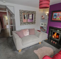 A living room with a fireplace a beige sofa pink cushions and a purple wall at Cherry Blossom Cottage in Stratford-Upon-Avon