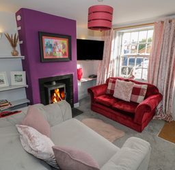 A living room with a red sofa and a white sofa near a fireplace with a purple wall at Cherry Blossom Cottage in Stratford-Upon-Avon