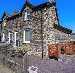 The exterior of a stone house with a blue door a small garden area and a wooden fence at Dola in Pentre Du near Betws-Y-Coed