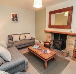 A living room with two sofas a wooden coffee table a stone fireplace with a wood stove a large wooden mirror and a wooden cabinet at Providence Cottage in Ugglebarnby near Sleights