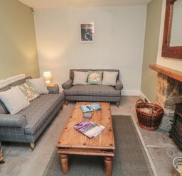 A living room with two gray sofas a wooden coffee table and a wood burning stove at Providence Cottage in Ugglebarnby near Sleights