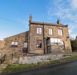 A stone house with multiple windows and chimneys on a sloped road at Providence Cottage in Ugglebarnby near Sleights
