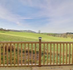 A wooden deck railing overlooking green fields and hills at Seren Lodge in Builth Wells