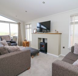 A living room with sofas a television on a mantle and large windows at Seren Lodge in Builth Wells