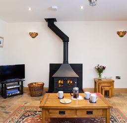 A living room with a wood burning stove and coffee table with cups and cookies at Teifi Cottage in Cardigan Near Cenarth
