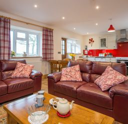 A living room with leather sofas and patterned cushions with a wooden coffee table and teapot in an open kitchen space at Teifi Cottage in Cardigan Near Cenarth
