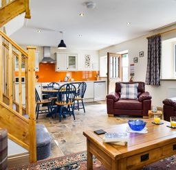 An open plan living area with kitchen dining table chairs leather armchairs and wooden staircase at Cych Cottage Cardigan Near Cenarth