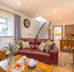A living room with leather sofas a wooden coffee table with a teapot and flowers and a dining table with chairs at Towy Cottage Cardigan Near Cenarth