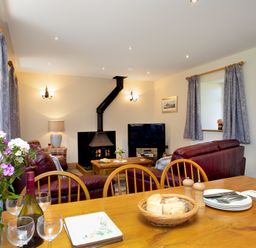A living room with a fireplace red sofas a wooden table with bread a bottle of wine and glasses at Towy Cottage Cardigan Near Cenarth