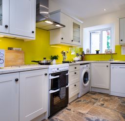 A kitchen with white cabinets yellow backsplash a stove microwave washing machine and dishwasher at Towy Cottage in Cardigan Near Cenarth