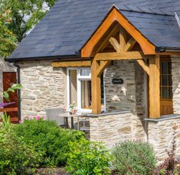 A stone cottage exterior with a wooden porch and garden furniture surrounded by plants and flowers at Gwaun Cottage Cardigan Near Cenarth