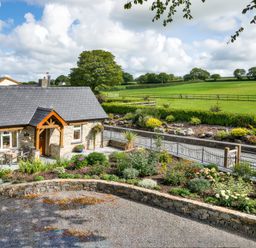 A stone cottage with a slate roof and garden in front of a green field at Gwaun Cottage Cardigan Near Cenarth