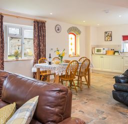 An open living room and kitchen with a dining table set with chairs and flowers at Cothi Cottage Cardigan Near Cenarth