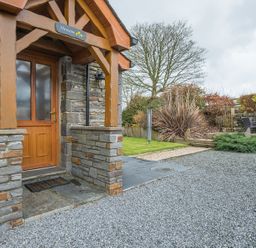 A stone and wood entrance door with a small covered porch and a gravel driveway and garden area at Hirwaun Cottage Cardigan Near Cenarth
