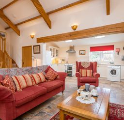 An open living room and kitchen with red sofa and armchair wooden beams and staircase at Hirwaun Cottage Cardigan Near Cenarth