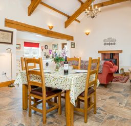 A dining area with wooden chairs and a table with a floral tablecloth next to a living room with sofas and a fireplace at Hirwaun Cottage Cardigan near Cenarth