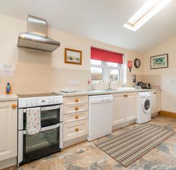A kitchen with white cabinets double oven dishwasher washing machine striped rug and wooden door at Hirwaun Cottage in Cardigan Near Cenarth