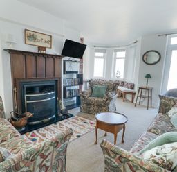 A living room with patterned sofas a wooden fireplace and a wall mounted TV at The Harbour in Rhosneigr
