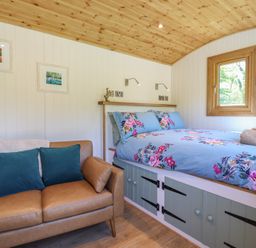 A bedroom with a floral bedspread a brown sofa and framed pictures on the wall at Celyn in Bontddu near Dolgellau