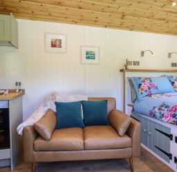 A small room with a brown leather sofa with blue cushions beside a bed with blue floral bedding at Celyn in Bontddu near Dolgellau