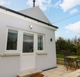 A small patio area with a wooden table and two chairs outside a white house at Orchard View in Pembroke