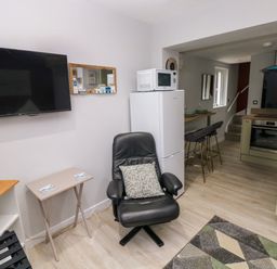A kitchen and living area with a black leather chair a white fridge with a microwave on top a wall mounted tv and a small dining table with bar stools at Orchard View in Pembroke
