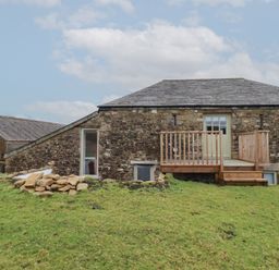 Stone barn with wooden deck door and steps on a grassy slope at Logan Barn in Poldue near Camelford