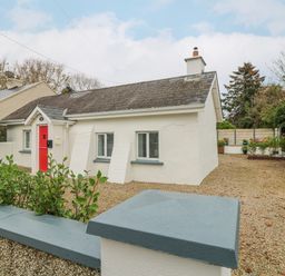 A small white house with a red door and a gravel driveway at Bayside Cottage in Rosslare Strand County Wexford