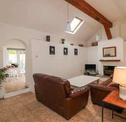 A living room with brown leather sofas a white coffee table a fireplace and a small TV next to an arched doorway at Bayside Cottage in Rosslare Strand County Wexford