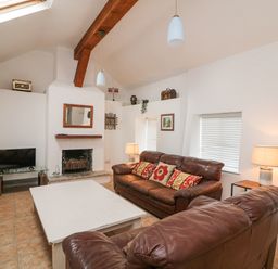 A living room with brown leather sofas a white coffee table a fireplace a TV on a glass stand lamps and a wall clock at Bayside Cottage Rosslare Strand County Wexford