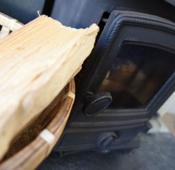 A close up of a wood burning stove and a wicker basket with firewood at Northern Lights in Polzeath