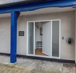 An entrance door open with a shoe rack visible inside and a blue painted post outside at Groves House in Castletown near Fortuneswell