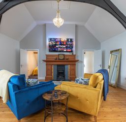 A living room with blue and yellow sofas facing a wooden fireplace and a wall-mounted TV at Groves House Castletown near Fortuneswell