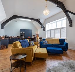 A living room with yellow and blue sofas a round side table wooden floor and an open kitchen with navy cabinets at Groves House Castletown near Fortuneswell