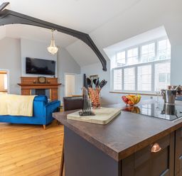 An open living room and kitchen area with a blue sofa wooden floor and a kitchen island with cooking utensils at Groves House in Castletown near Fortuneswell