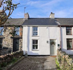A row of stone and white painted terraced houses with paved driveways and a tree in front at Cwrt Dwyran near Niwbwrch Newborough